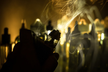 Vape concept. Electronic Cigarette vape explosion. Smoke clouds and vape liquid bottles on dark...