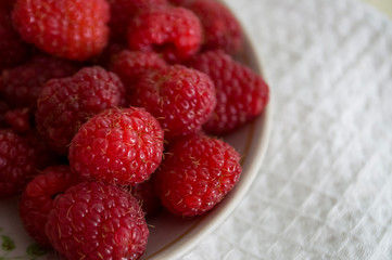 Big ripe raspberries are laying on the  table covered with white tablecloth