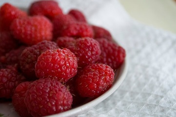 Big ripe raspberries are laying on the  table covered with white tablecloth