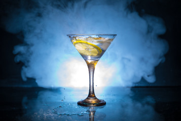 Martini cocktail glass in hand splashing on dark toned smoky background or colorful cocktail in glass with splashes and olives. Party club entertainment. Mixed light. Selective focus
