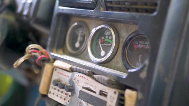 Interior dashboard, radio and gauges of a beat up old vehicle. Wires sticking out of the dash and keys dangling from the ignition switch. View inside driver compartment of old truck. DOLLY LEFT.