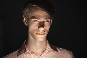 Close-up portrait of Caucasian attractive young man blinked his eyes. light shines from below. Standing Isolated on black background and looking at camera. Fear concept