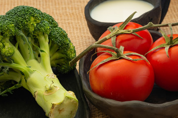 Organic vegetables tomato broccoli  black clay bowl and milk black clay cruise on jute cloth tablecloth, healthy concept