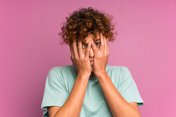 Young african american man over isolated purple wall covering eyes and looking through fingers