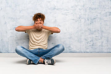 Young african american man sitting on the floor covering mouth with hands