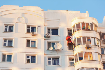 Industrial climber fixed on safety ropes puttying and painting the facade of building on sunny day. Bottom view from afar.