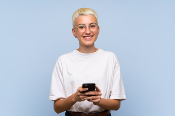 Teenager girl with white short hair over blue wall sending a message with the mobile