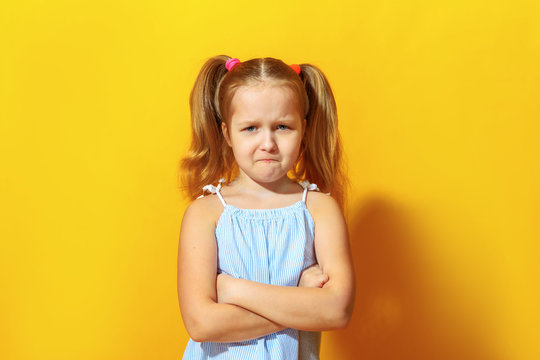 Closeup portrait of upset little girl on yellow background. The child crossed his arms and pouted his lips.