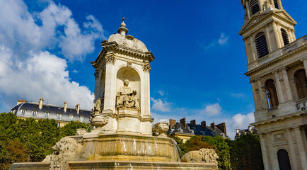 Fototapeta na wymiar Fountain in front of the church of Saint-Sulpice in cloudy blue sky day in Paris, France