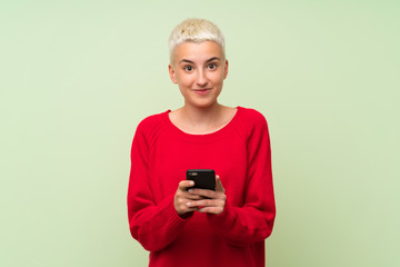 Teenager girl with white short hair over green wall sending a message with the mobile