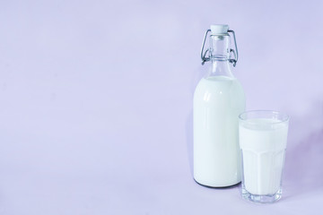 Fresh milk for breakfast in a glass bottle and a glass of milk on a lavender background