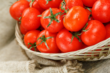 Ripe and juicy cherry tomatoes with drops of moisture in a wicker basket. Old wooden table, around the canvas of burlap