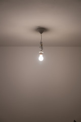 naked lit light bulb hanging from the ceiling of a dimly lit room