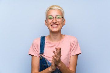 Teenager girl with overalls on blue wall applauding