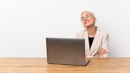 Teenager girl with short hair with a laptop looking up while smiling