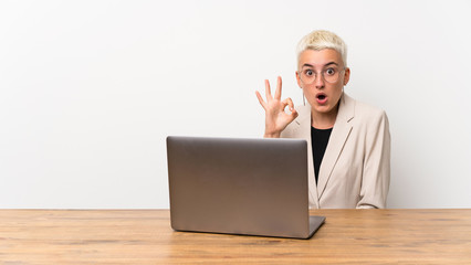 Teenager girl with short hair with a laptop surprised and showing ok sign