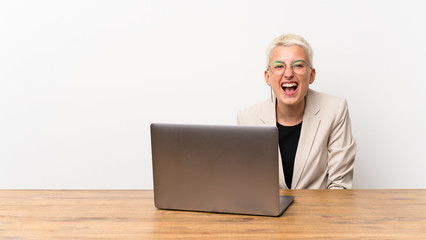 Teenager girl with short hair with a laptop shouting to the front with mouth wide open