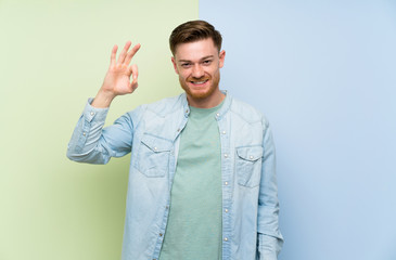 Redhead man over colorful background showing ok sign with fingers