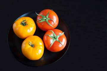 Red and yellow tomatoes on a black plate