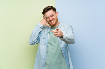 Redhead man over colorful background making phone gesture and pointing front