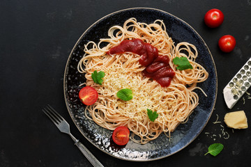 Italian food, traditional pasta spaghetti with tomato sauce, parmesan cheese and greens on a black stone background. Top view, flat lay