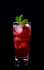 Red drink with ice, raspberries and mint in a tall glass against the black background