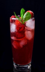 Red drink with ice, raspberries and mint in a tall glass against the black background