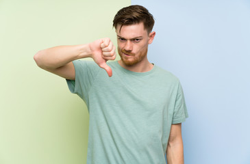 Redhead man over colorful background showing thumb down sign