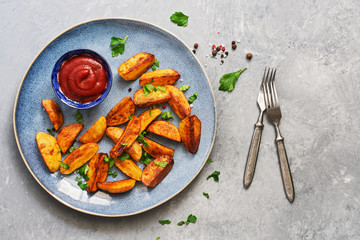 Fried potatoes with tomato sauce, spices and greens in a plate on a gray background. Top view, copy space.