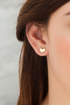 Oreja de mujer con aretes de corazon, pelo ca&oacute;tico y piel suave