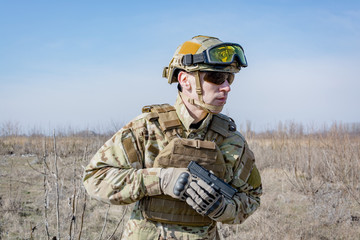 Male soldier in nato uniform with hand gun outoors in the field