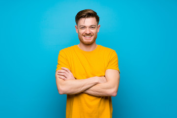 Redhead man over blue wall keeping the arms crossed in frontal position