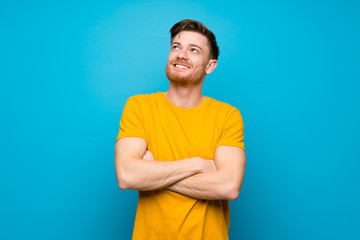 Redhead man over blue wall looking up while smiling