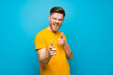 Redhead man over blue wall pointing to the front and smiling