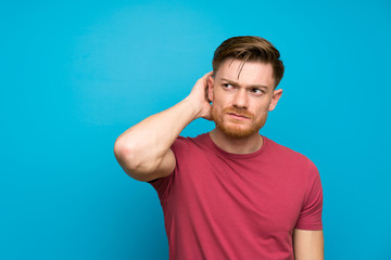 Naklejka premium Redhead man on isolated blue wall having doubts and with confuse face expression