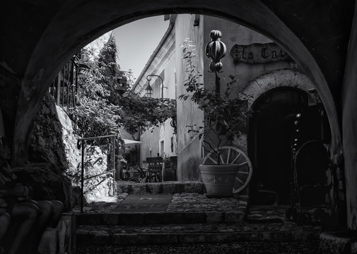 Black and white photo  of the entrance to the La Caverne restaurant in a narrow street in the old center of the  picturesque medieval village of Eze