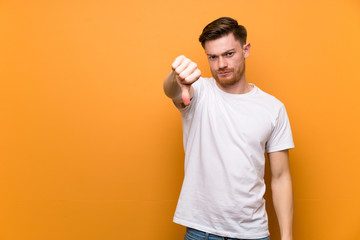 Redhead man over brown wall showing thumb down with negative expression