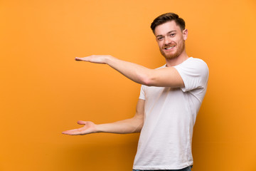 Redhead man over brown wall holding copyspace to insert an ad