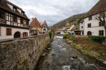 The mountain river flows through the old town. On the banks there are half-timbered houses with tiled roofs. France. Alsace. Kaysersberg.
