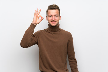 Fototapeta premium Blonde man over isolated white wall showing an ok sign with fingers