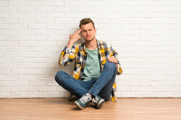 Blonde man sitting on the floor with problems making suicide gesture