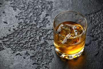 Glass of whiskey with ice on rustic background