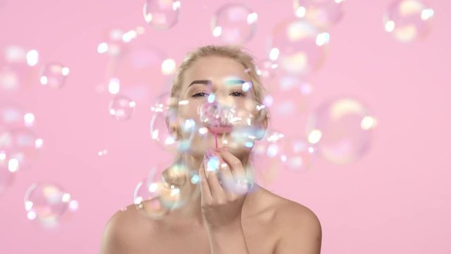 Young positive woman blowing soap bubbles and smiling.