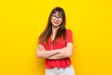 Young woman over yellow wall keeping the arms crossed in frontal position