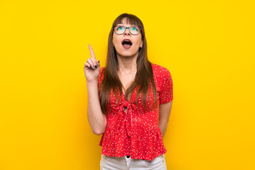 Young woman over yellow wall pointing up and surprised