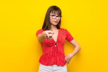 Young woman over yellow wall points finger at you with a confident expression