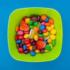 Multicolored round candies in a plate on blue background top view
