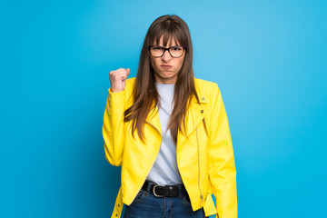 Young woman with yellow jacket on blue background with angry gesture