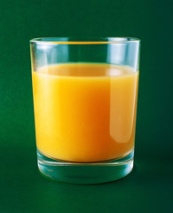 Glass with orange juice on a green background