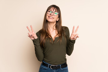 Young woman on ocher background showing victory sign with both hands